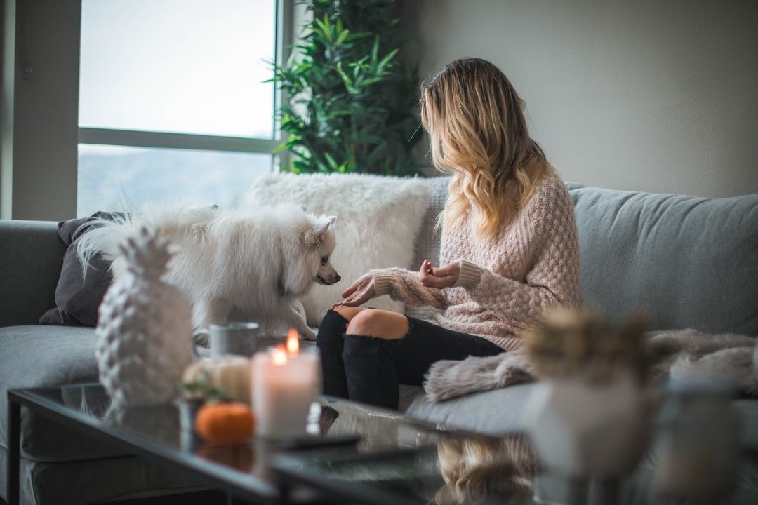 Kvinna i varm tröja sitter med en liten hund i ett mysigt vardagsrum